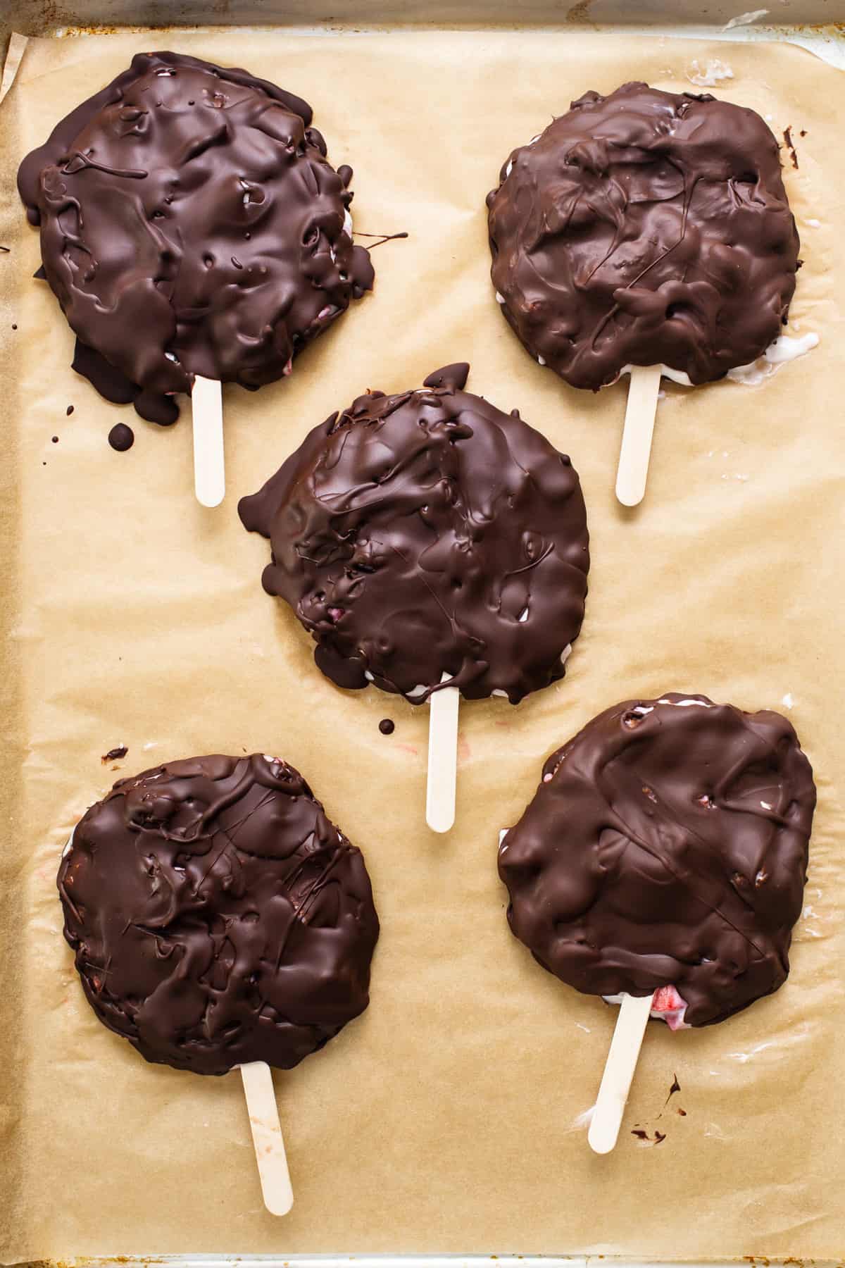 Chocolate covered popsicles on a baking sheet.