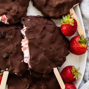 Chocolate covered strawberry popsicles on a plate.