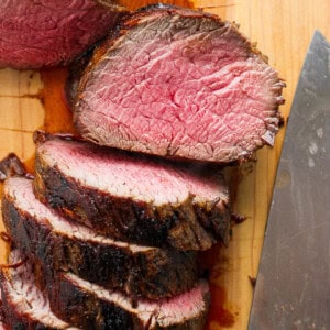 Sliced steak on a cutting board with a knife.