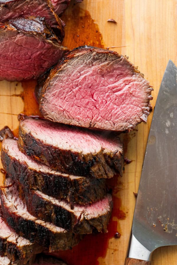 Sliced steak on a cutting board with a knife.