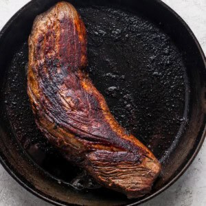 A steak is being cooked in a cast iron skillet.