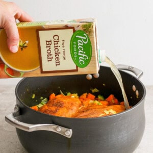 A person pouring a bottle of liquid into a pan.