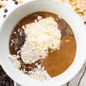 A white bowl with ingredients for a peanut butter chocolate chip cookie.