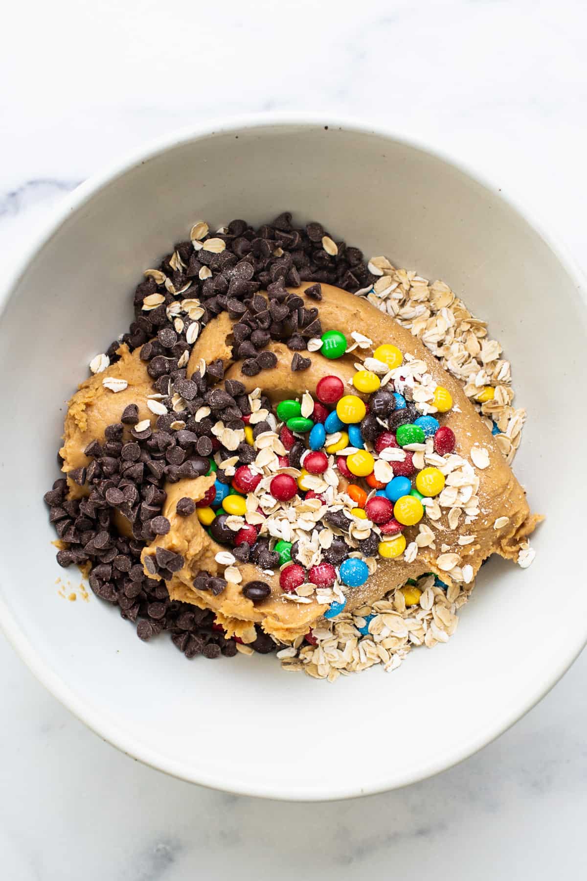 A white bowl filled with granola, oats and chocolate chips.