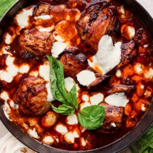 A skillet with chicken in a sauce with basil leaves.