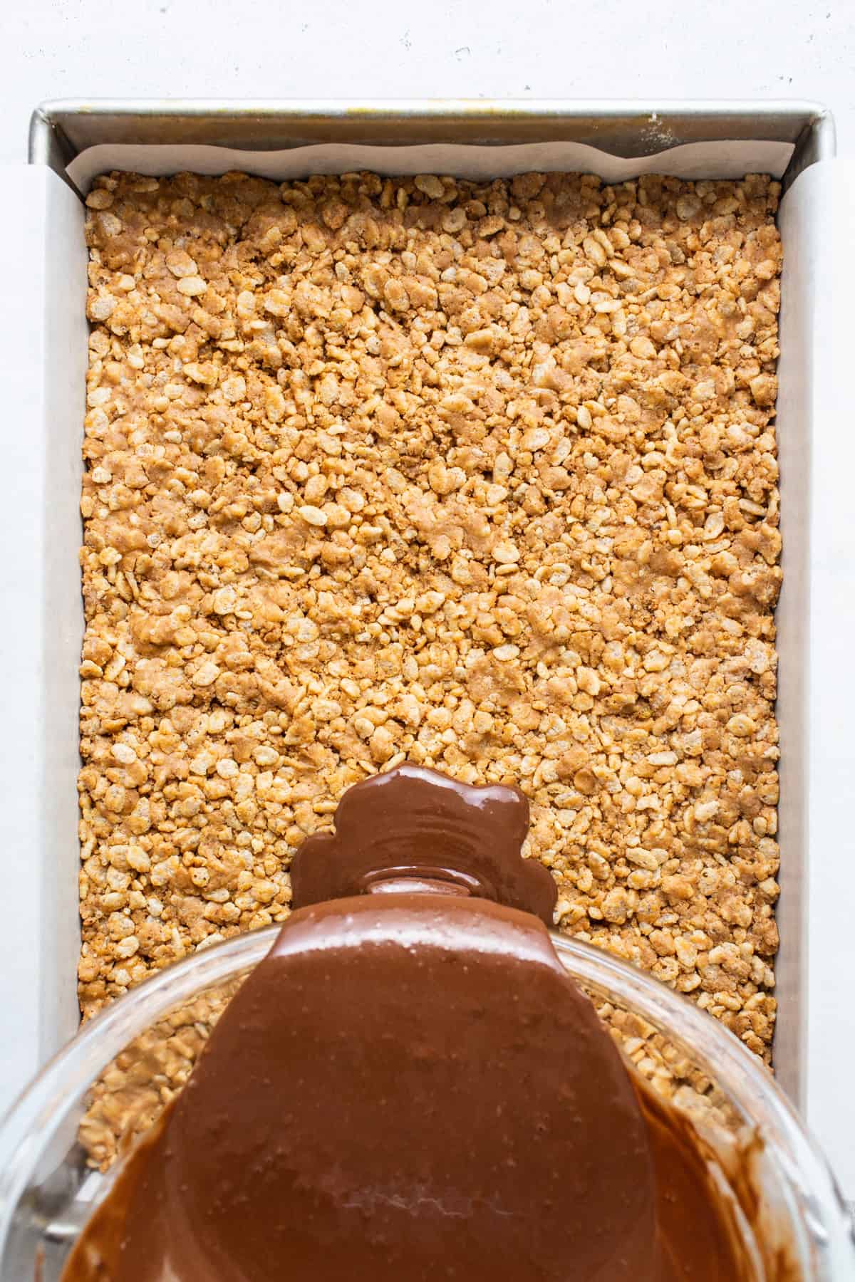 A chocolate sauce being poured over oats in a baking dish.