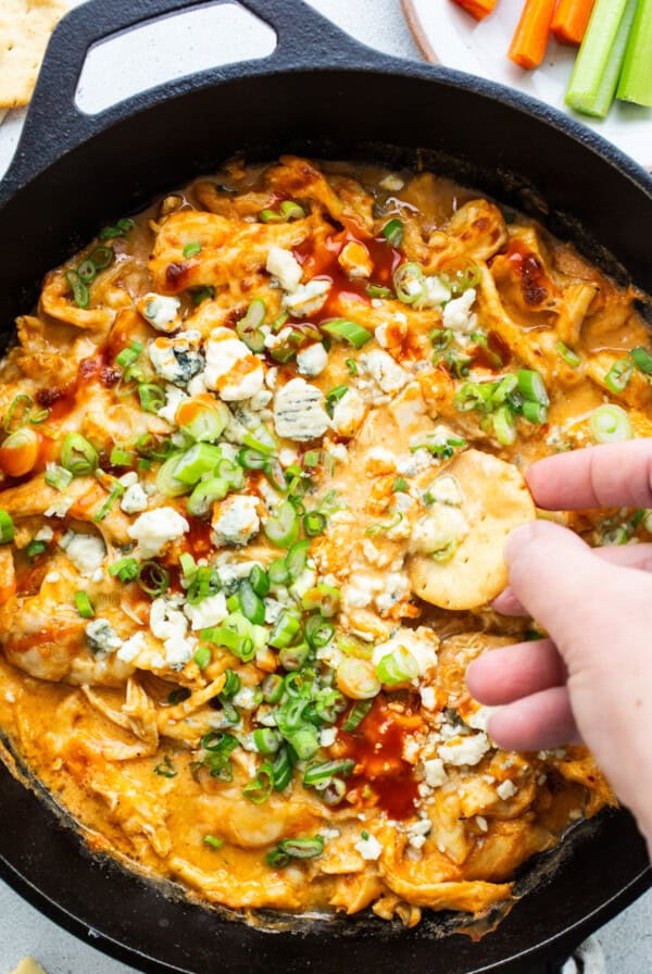 A person dipping into a skillet of buffalo chicken dip.