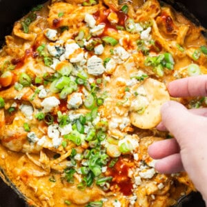 A person dipping chips into a bowl of buffalo chicken dip.