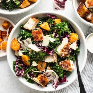 A bowl of chicken kale salad with dressing.