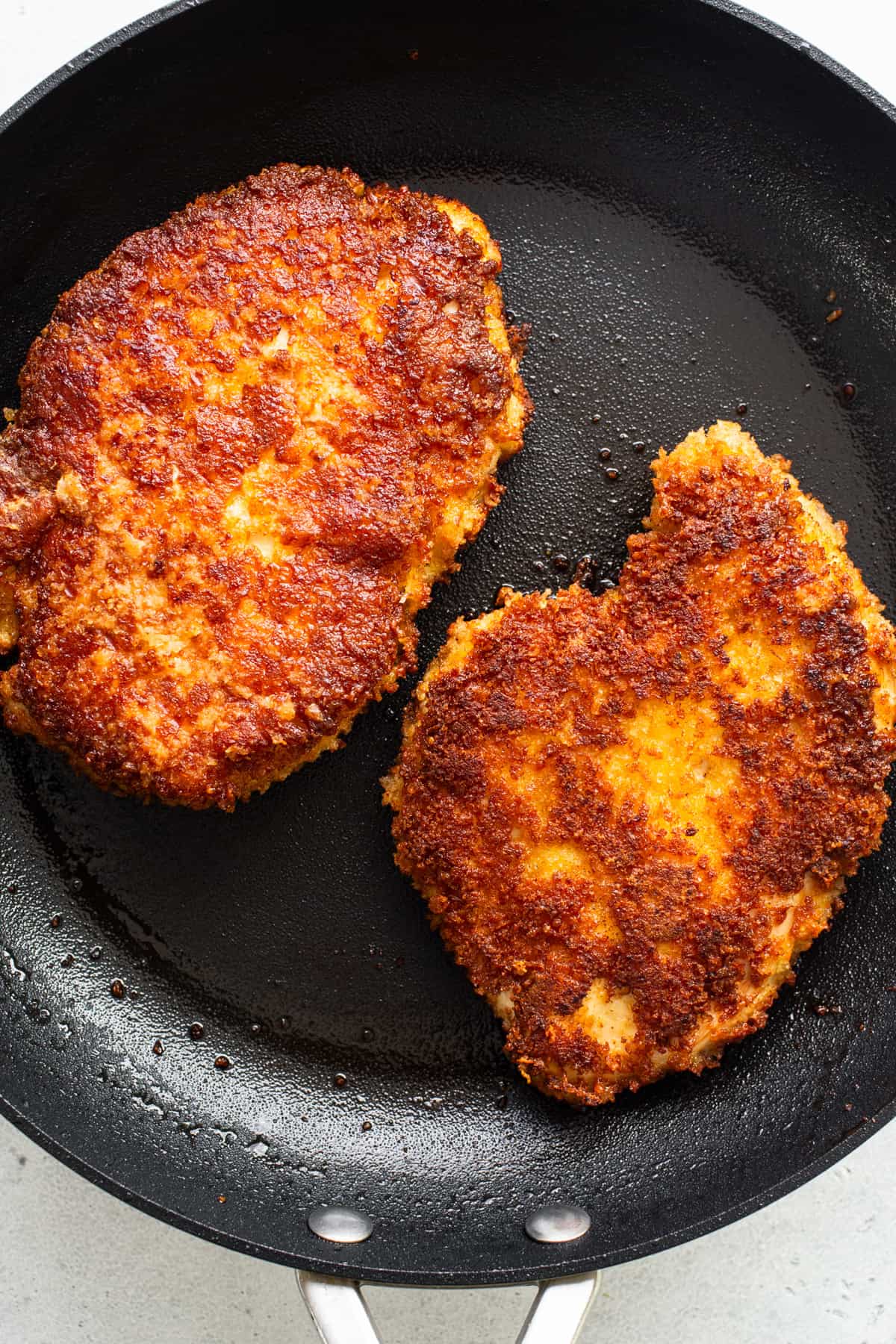 Two fried chicken patties in a frying pan.