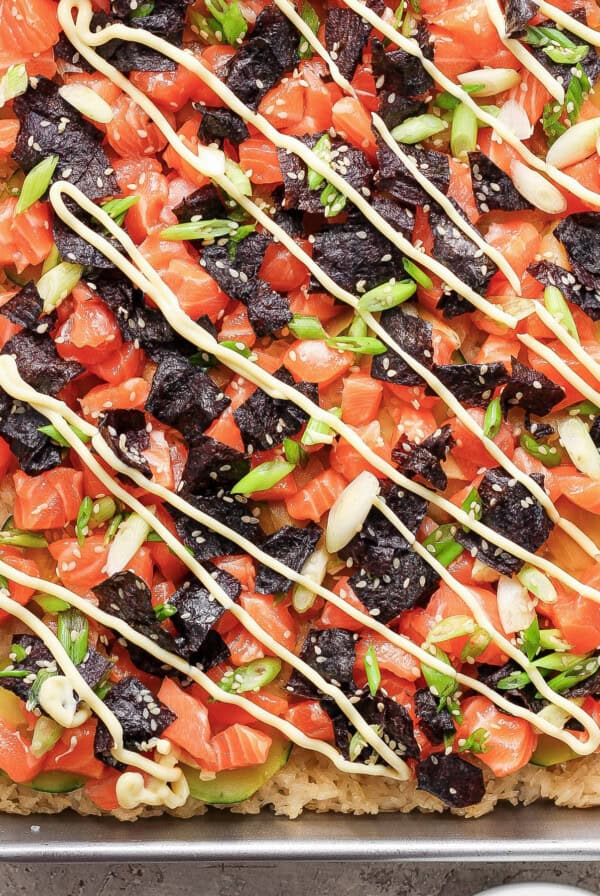 A pizza with salmon, avocado, and arugula on a baking sheet.