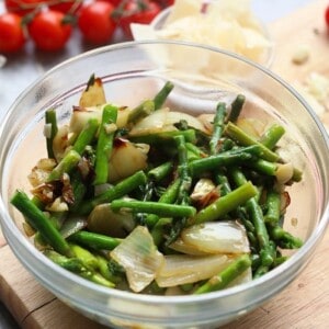 A bowl of shrimp scampi with asparagus on a cutting board.