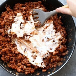 A person pouring cream into a frying pan to prepare a delicious chili cheese dip.