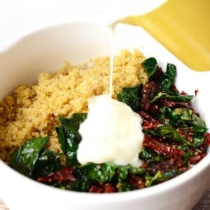 A bowl of spinach and quinoa with cream being poured over it, creating a nutritious and delicious twist on quinoa mac n' cheese.