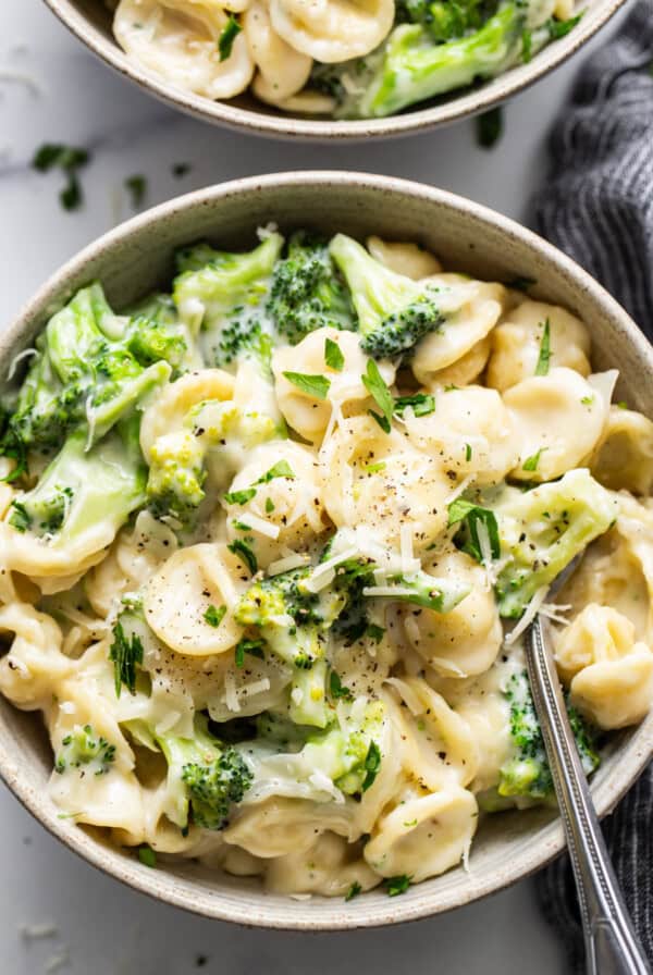 Two bowls of pasta with broccoli and parmesan cheese.