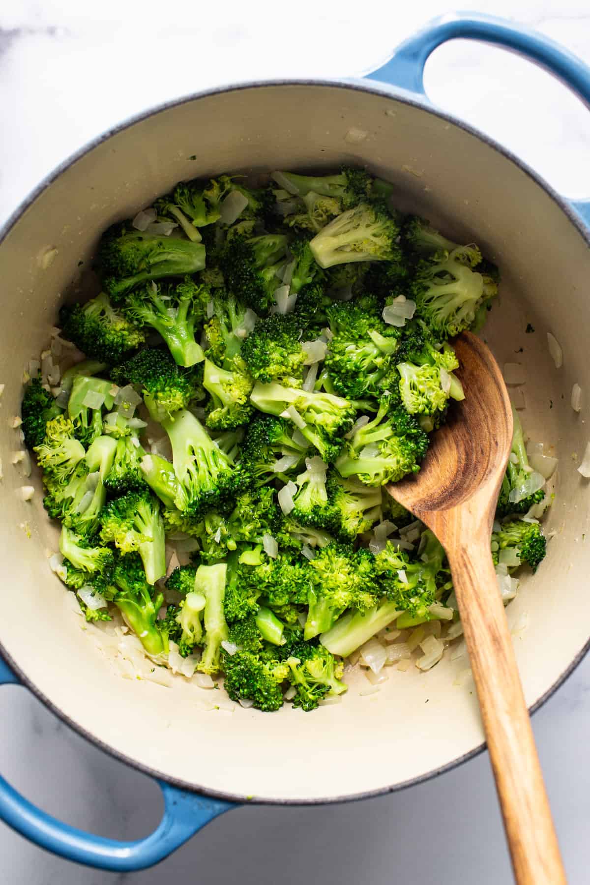 Broccoli in a blue pot with a wooden spoon.