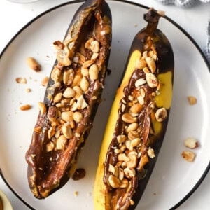 Two bananas with peanuts and chocolate on a plate.