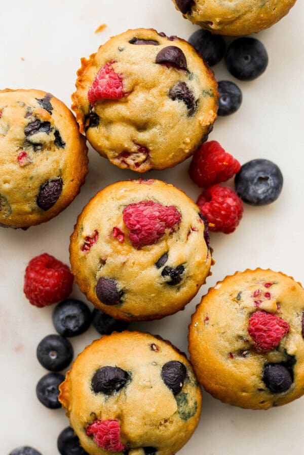 A group of muffins with raspberries and blueberries on top.