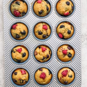 Muffins in a muffin tin with raspberries and blueberries.