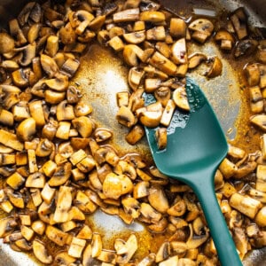 Mushrooms in a pan with a green spatula.