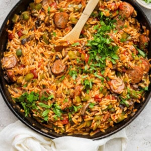 A skillet full of rice and vegetables with a wooden spoon.