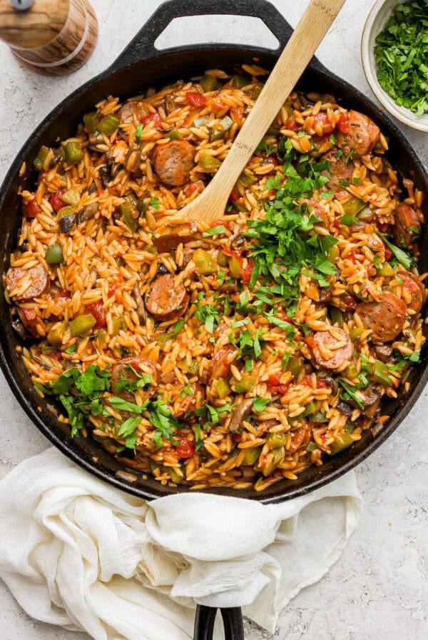 A skillet full of rice and vegetables with a wooden spoon.