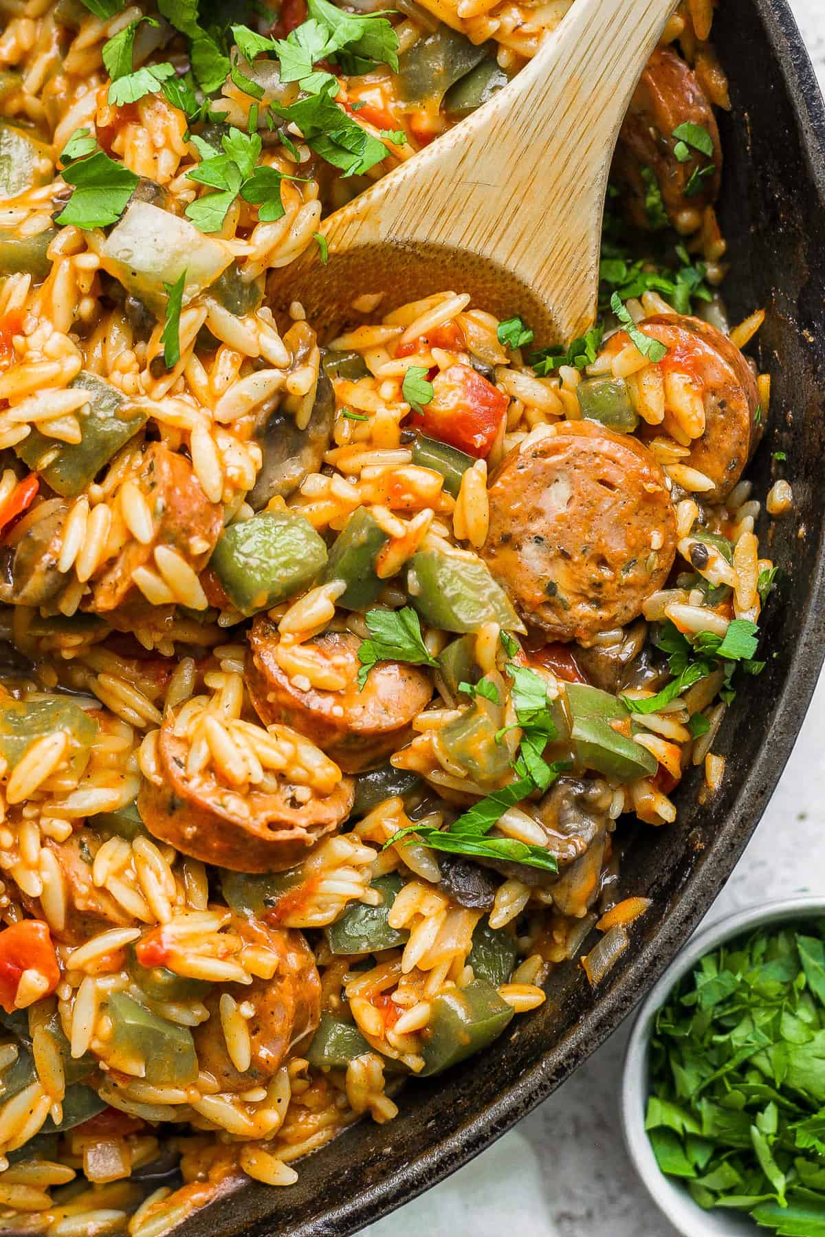 Sausage and rice in a skillet with a wooden spoon.