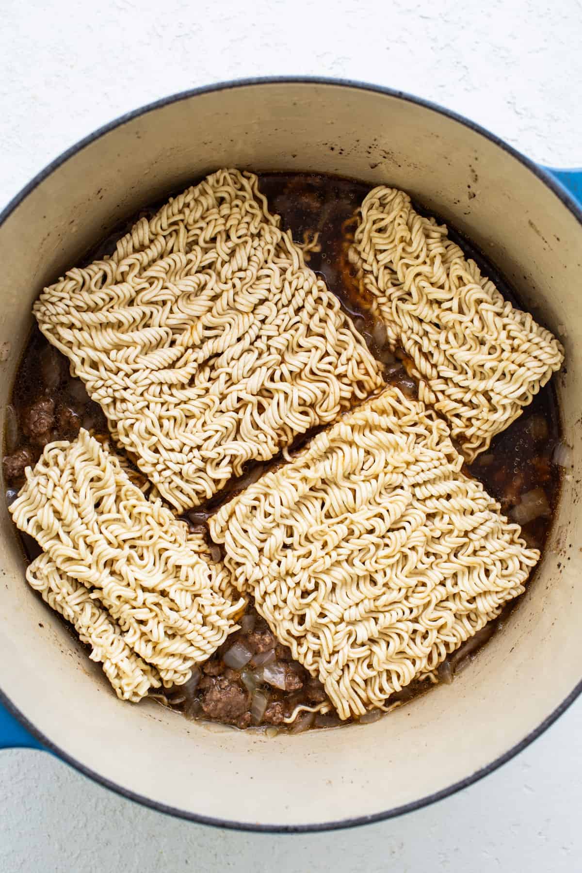 Ramen noodles in a pot on a white surface.