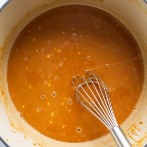 A pot of sauce with a whisk in it.