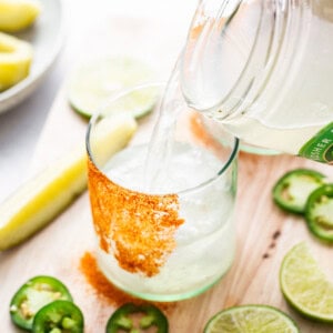 A person pouring a drink into a glass with limes and jalapenos.