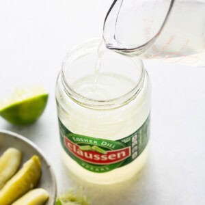 A person pouring a liquid into a jar of pickles.