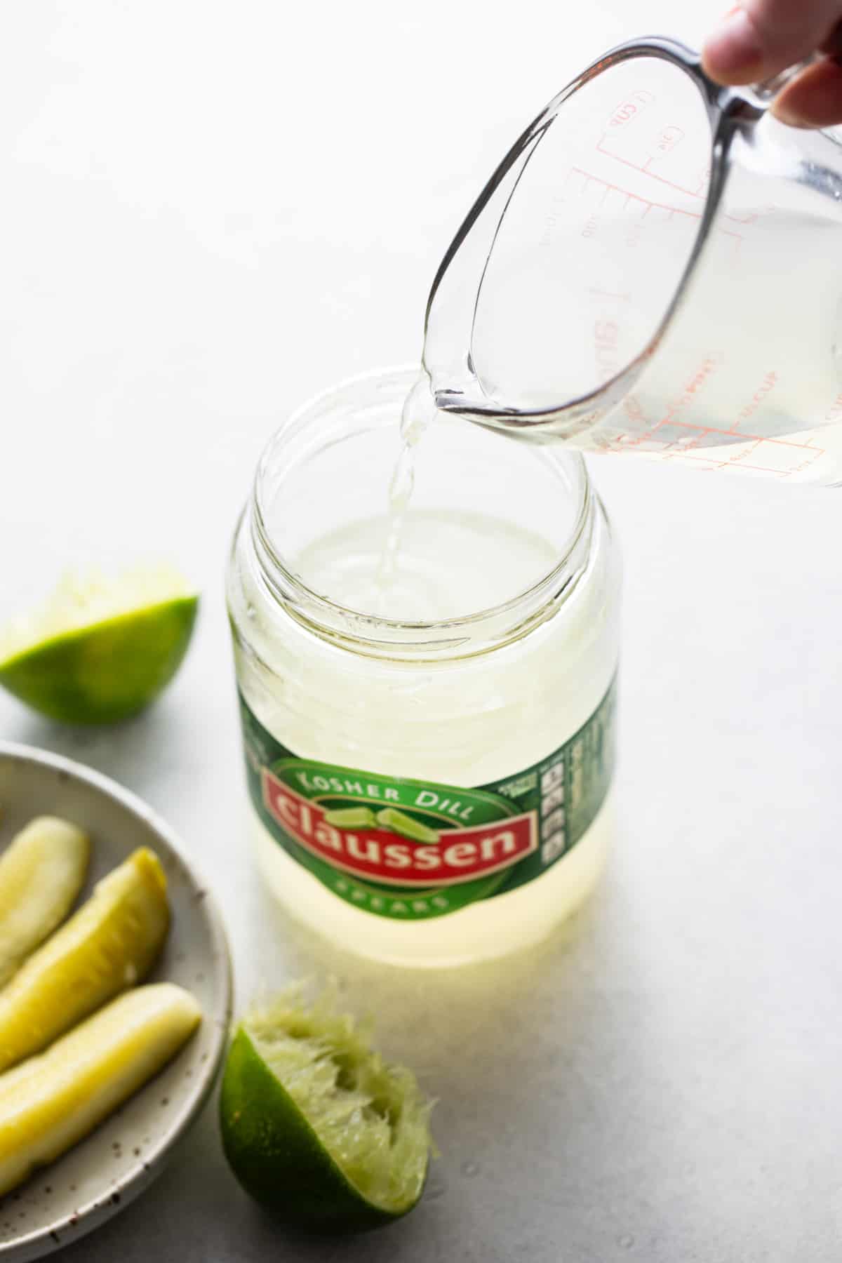 A person pouring a liquid into a jar of pickles.