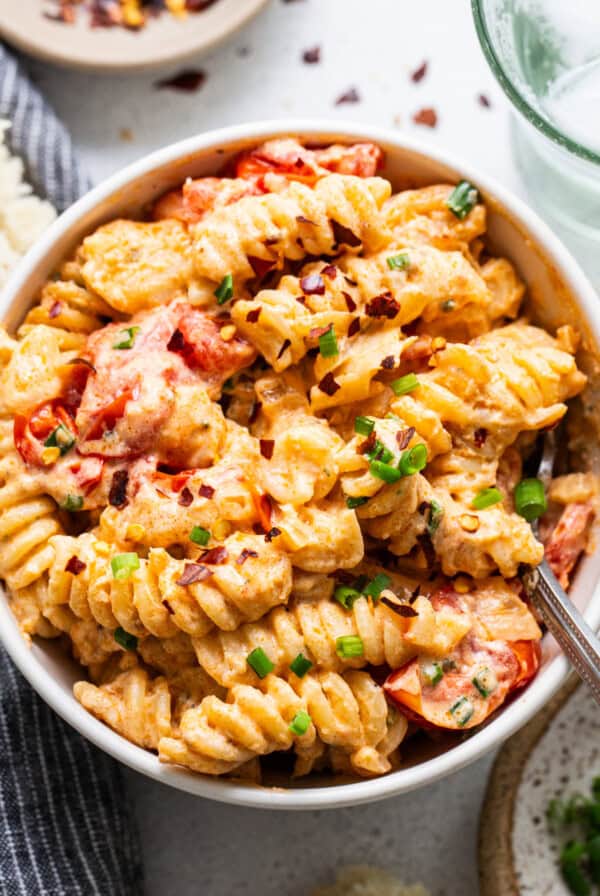 A bowl of creamy baked macaroni and cheese with sliced tomatoes and chopped green onions on top.