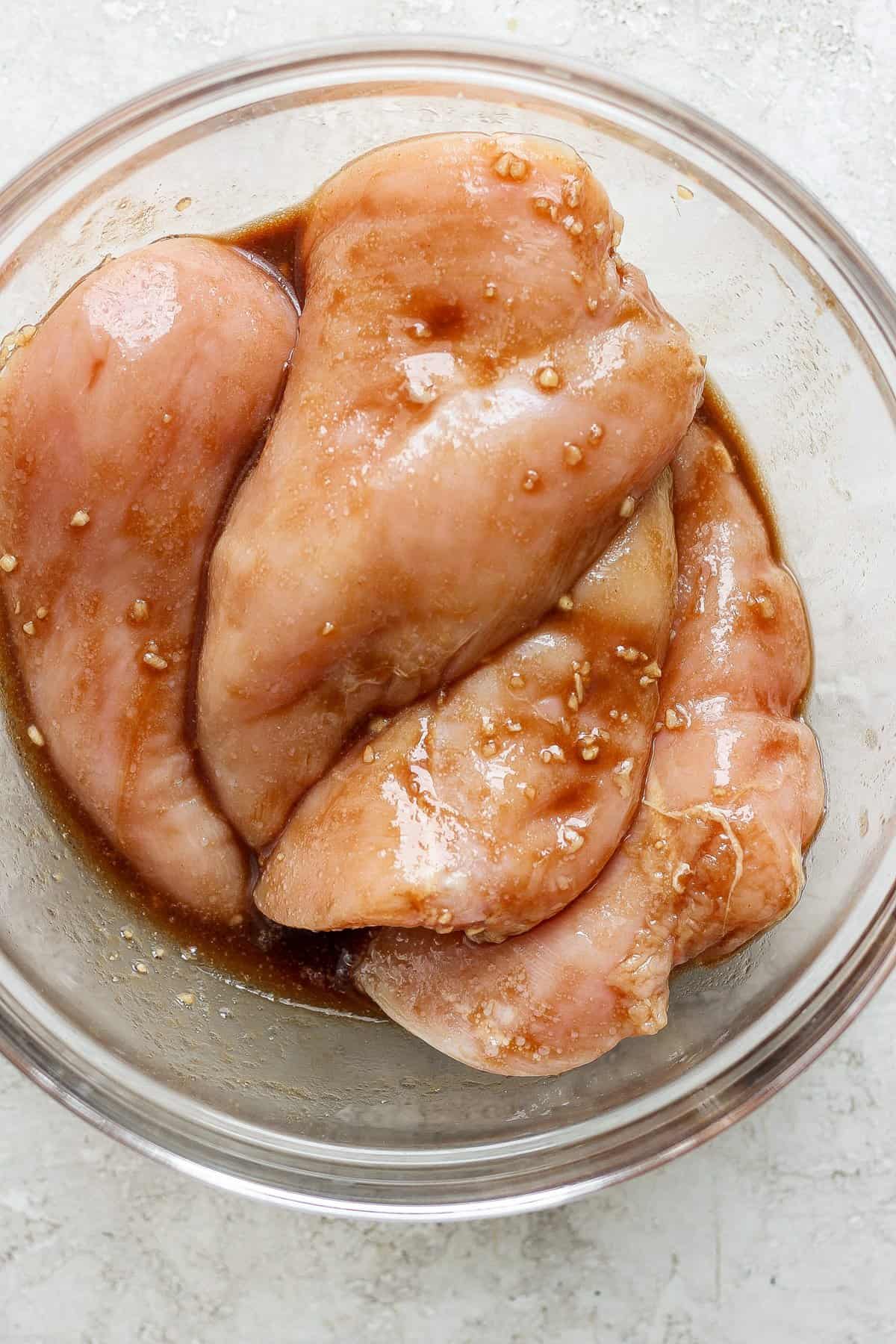 Raw chicken breasts marinating in a seasoned sauce.