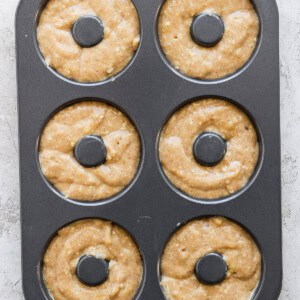 A six-cavity donut baking pan filled with raw donut batter, ready to be baked.