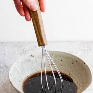 A hand whisking a liquid mixture in a ceramic bowl.