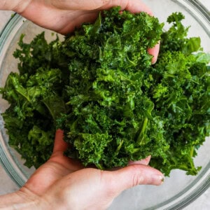 Hands holding fresh kale above a glass bowl.