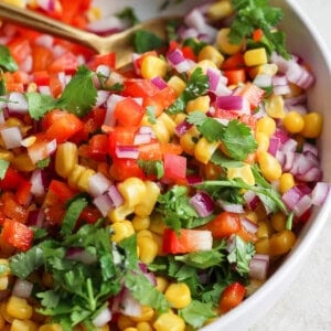 A vibrant bowl of corn salsa with diced red onions, chopped tomatoes, and fresh cilantro.