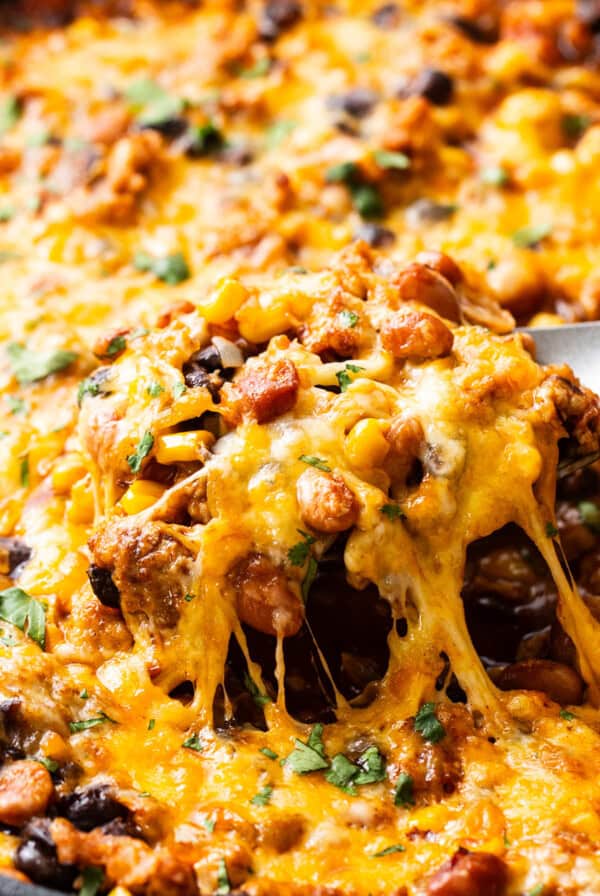 A skillet with melted cheese being lifted, revealing a cheesy, bean and meat mixture beneath.