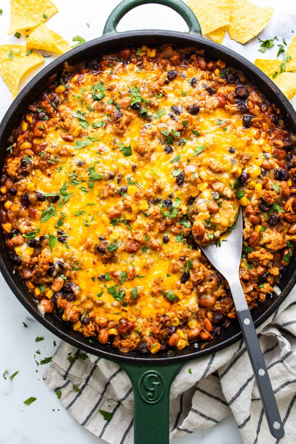 A skillet of baked cheesy chili with a side of tortilla chips.