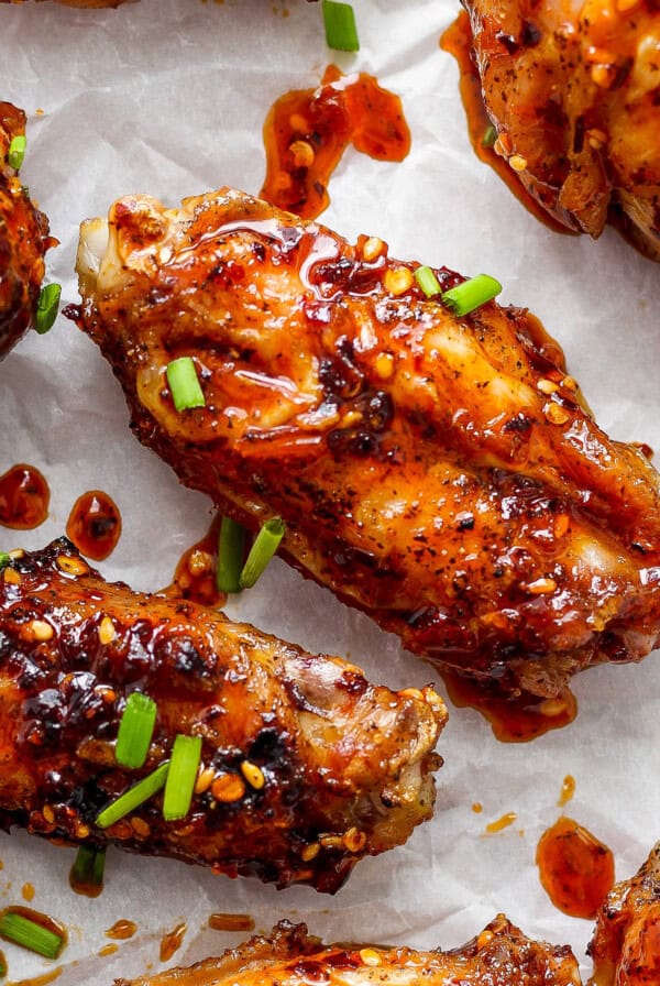 Glazed chicken wings on parchment paper garnished with sesame seeds and chopped green onions.