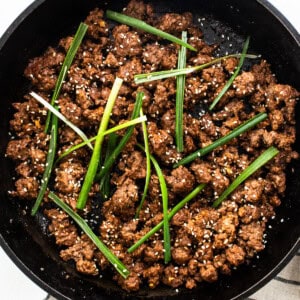 Cooked Korean ground beef garnished with green onions and sesame seeds in a cast iron skillet.