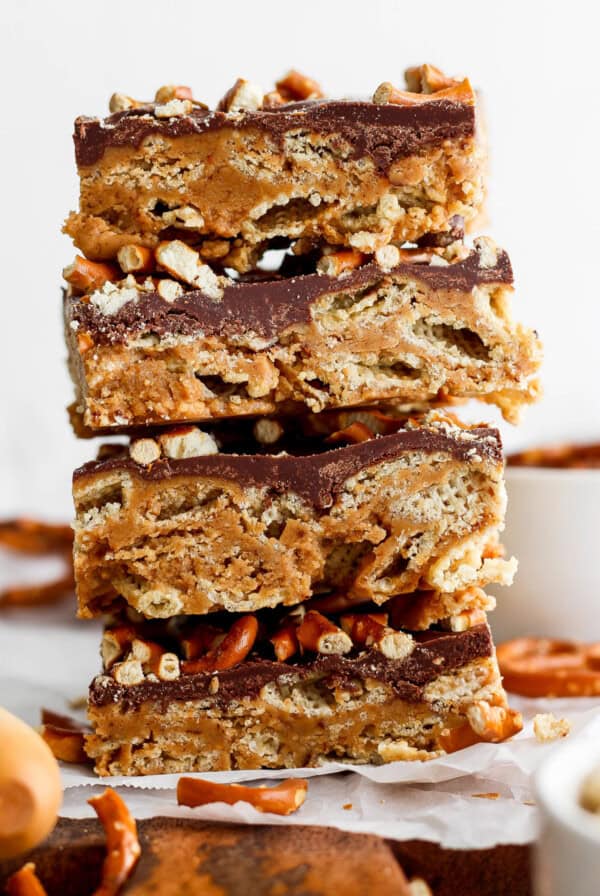 A stack of three layered peanut butter bars with a chocolate topping and crushed nuts on parchment paper.