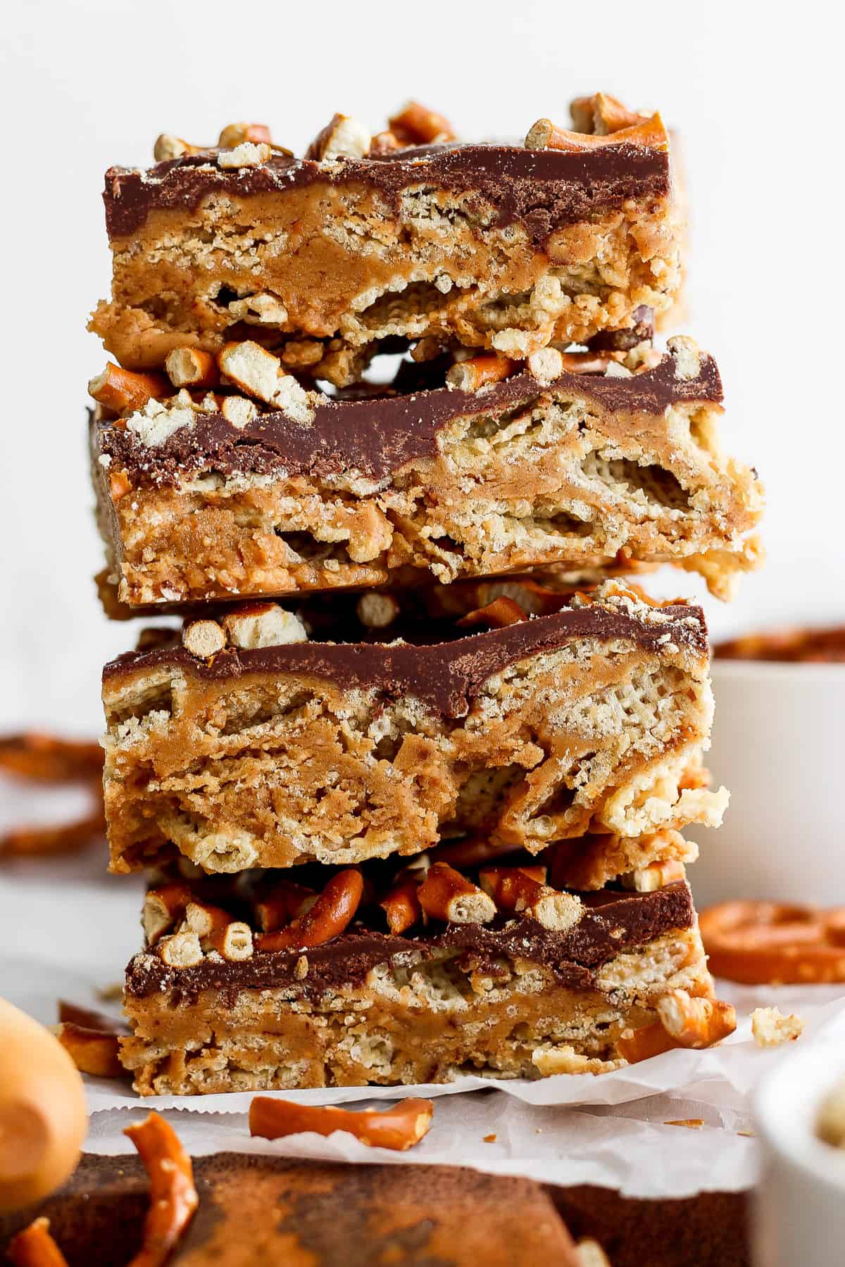 A stack of three layered peanut butter bars with a chocolate topping and crushed nuts on parchment paper.