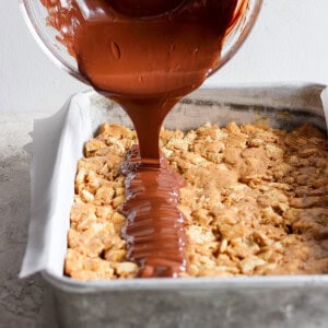 Chocolate sauce being poured onto a tray of baked dessert bars.