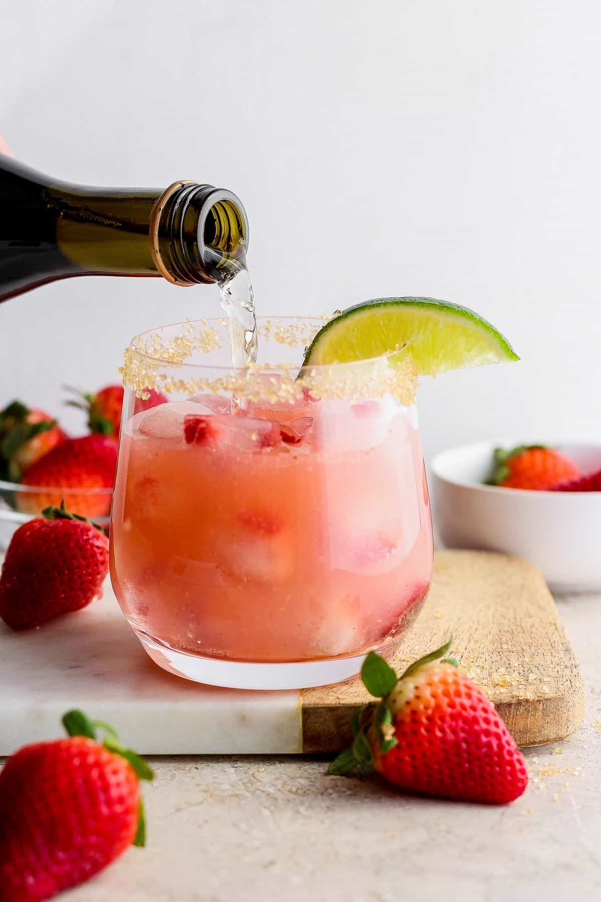 Pouring a drink into a strawberry cocktail garnished with a lime slice.