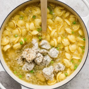 Pot of chicken noodle soup with green peas and a wooden spoon.