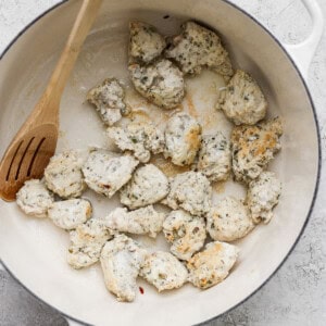 Chicken pieces being cooked in a white pot with a wooden spoon.