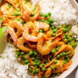 A bowl of white rice topped with shrimp and green peas in a creamy sauce, garnished with a lime wedge.