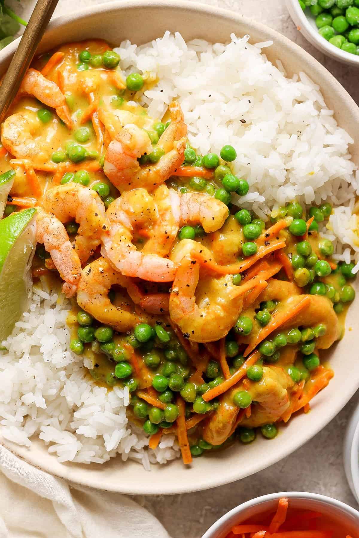 A bowl of white rice topped with shrimp and green peas in a creamy sauce, garnished with a lime wedge.